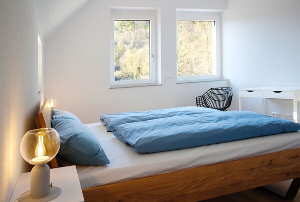 A bedroom with a bed, two windows, a bedside lamp, a chair, and a white dresser. - Spacious apartment 8 with use of sauna (Herbolzheim)