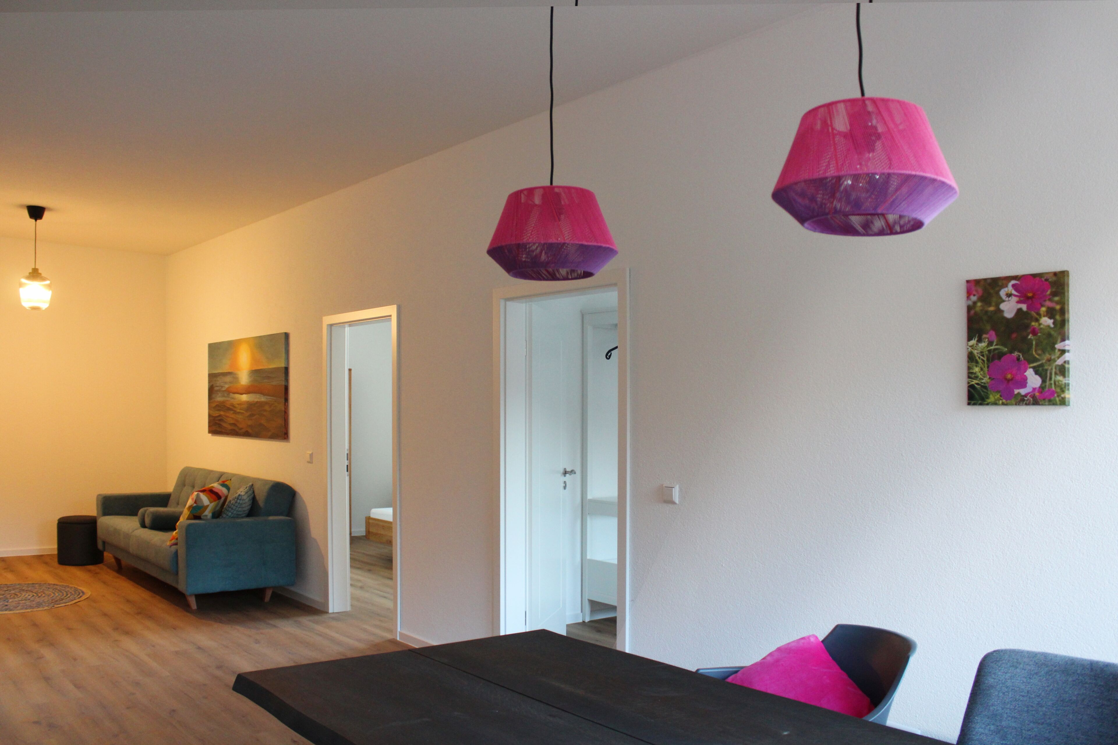 A modern living room with a sofa, a dining table, and a kitchen area visible through an open door.