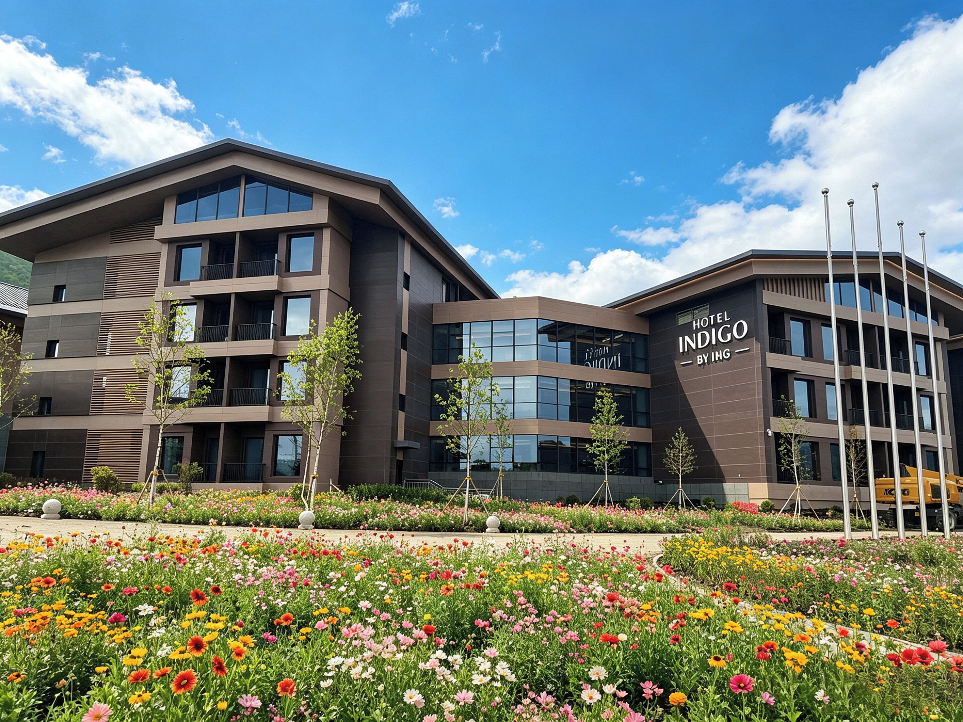 A modern hotel building with multiple floors, balconies, and a landscaped garden with colorful flowers.