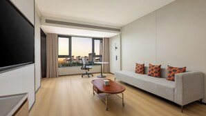 Ein modernes Hotelzimmer mit großem Fenster, einer Couch, einem Schreibtisch und einem Flachbildfernseher.
