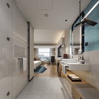 A modern hotel room with a large bed, a sitting area, a bathroom with a mirror and sink, and a view of the city.