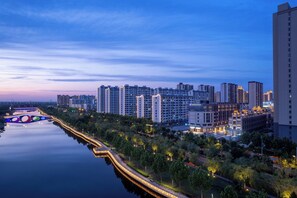 A high-rise hotel with multiple floors, a well-lit waterfront promenade, and a bridge in the background.