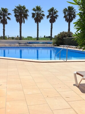 Ein Schwimmbecken mit klarem, blauem Wasser, umgeben von Palmen und einer gefliesten Terrasse.