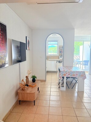 Eine moderne Küche mit Essbereich, einem an der Wand montierten Fernseher und Blick durch einen Bogen.