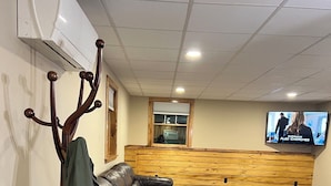Een moderne woonkamer met een hoekbank, een kapstok en een aan de muur bevestigde televisie.