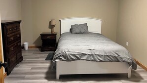 Een slaapkamer met een bed, een dressoir, nachtkastje, lamp en een stopcontact.