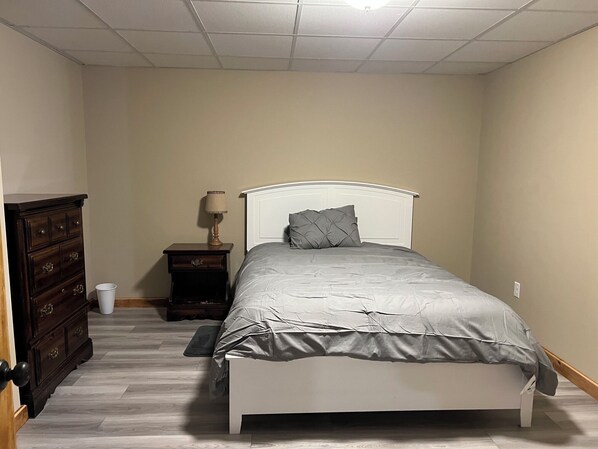 Un dormitorio con cama, cómoda, mesita de noche, lámpara y enchufe.
