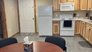 Een keuken met houten kastjes, een witte koelkast, een magnetron, een oven en een eettafel met stoelen.