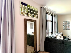 A room with a large window, a mirror, a sofa, and a wall-mounted scoreboard. - The Dugout - Baseball Oasis Duplex Condo (Dyersville)