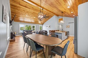 Una cucina moderna con isola centrale, un'area pranzo con un grande tavolo ovale e un soffitto a loft con travi in legno.