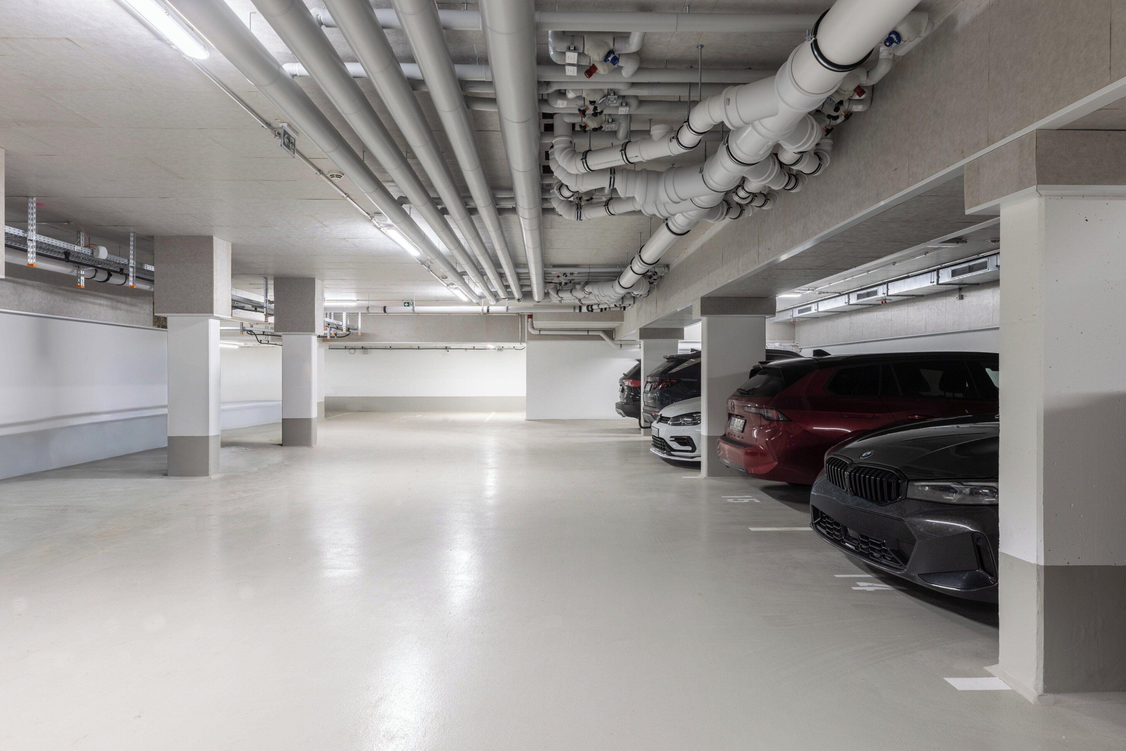Un estacionamiento de varios niveles con pilares de hormigón y tuberías en el techo.