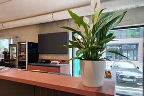 A reception area with a potted plant, a flat-screen TV, and a view of the street outside. - Holiday Inn - the niu, Clink Hamburg Barmbek by IHG (Hamburg)