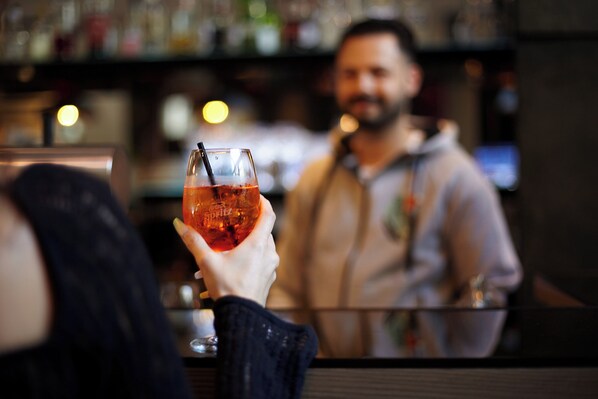 A person holding a glass with a straw, a blurred background with a bar counter and shelves. - Holiday Inn - the niu, Clink Hamburg Barmbek by IHG (Hamburg)