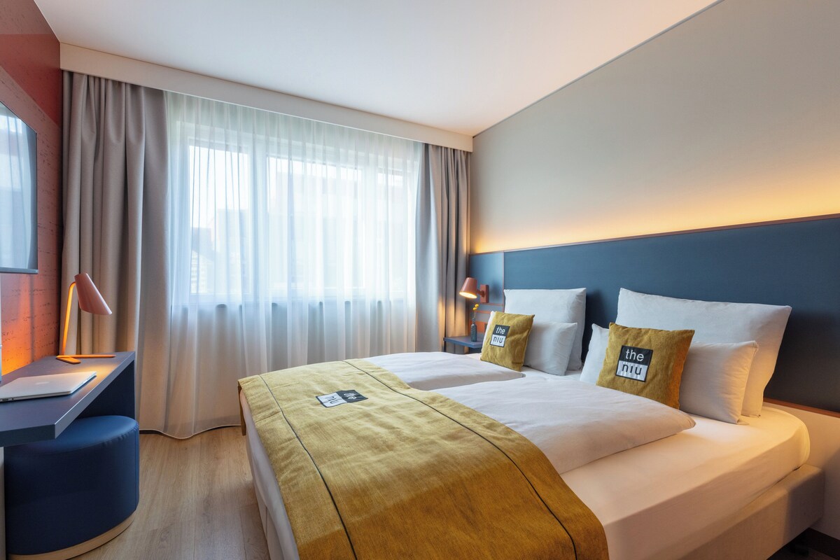 A hotel room with a bed, a desk, a lamp, and a window with curtains.