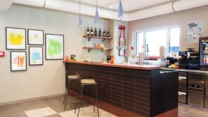 A bar area with stools, a counter, and framed artwork on the wall. - Holiday Inn - the niu, Clink Hamburg Barmbek by IHG (Hamburg)
