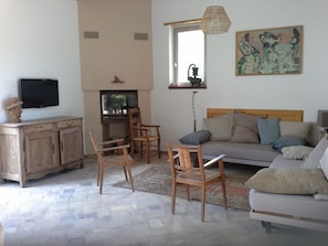 Un salon avec un canapé, des fauteuils, un téléviseur, une fenêtre et des œuvres d’art accrochées au mur.