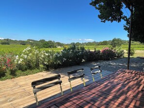 Une terrasse en bois, agrémentée de bancs, qui offre une vue sur un jardin aménagé et des champs.