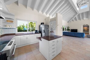 A spacious kitchen with white cabinets, a large window, and a blue sofa in the living area. - Casa Doce – Charming Ocean View Villa with Private Pool (Kralendijk)