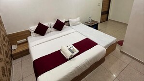 A hotel room with a large bed, a ceiling fan, a bedside table with a phone, and a door leading to another room. - Hotel Yuvraj (Gandhinagar)
