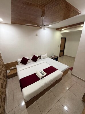 Habitación de hotel con una cama grande, un ventilador de techo, una mesita de noche con teléfono y una puerta que da a otra habitación.