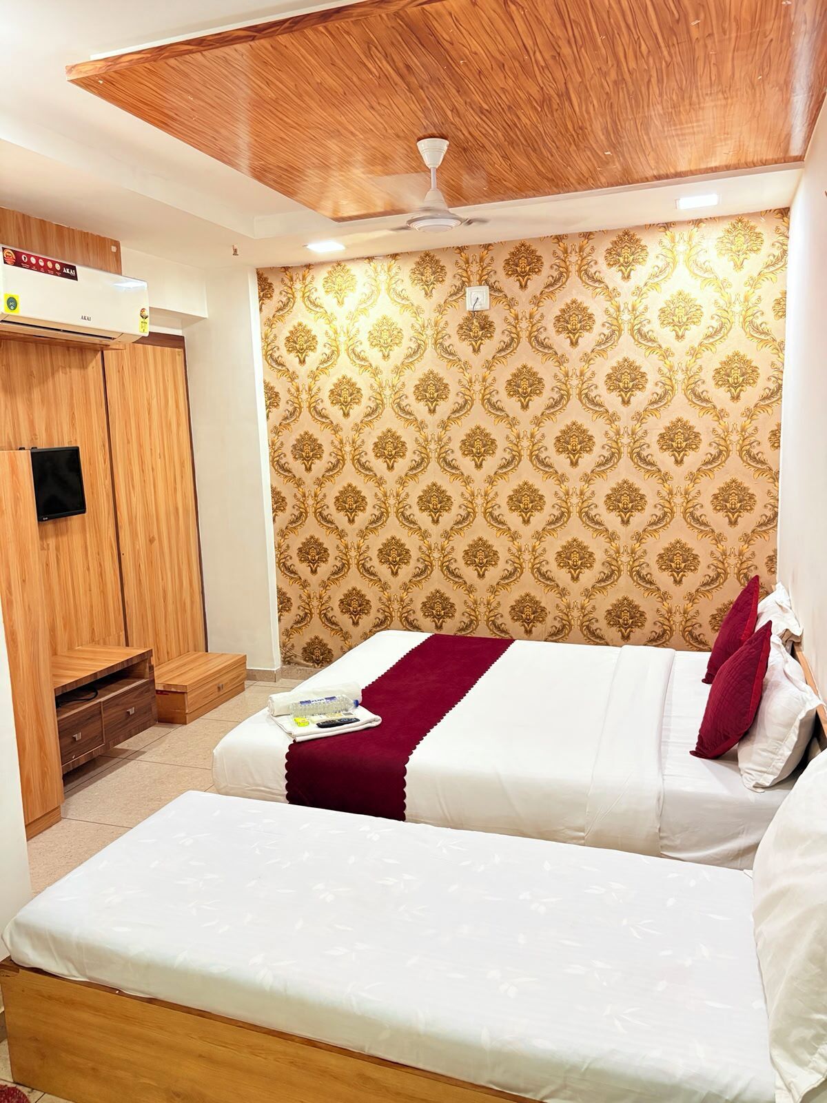 A bedroom with two beds, a wooden wardrobe, a ceiling fan, and patterned wallpaper.