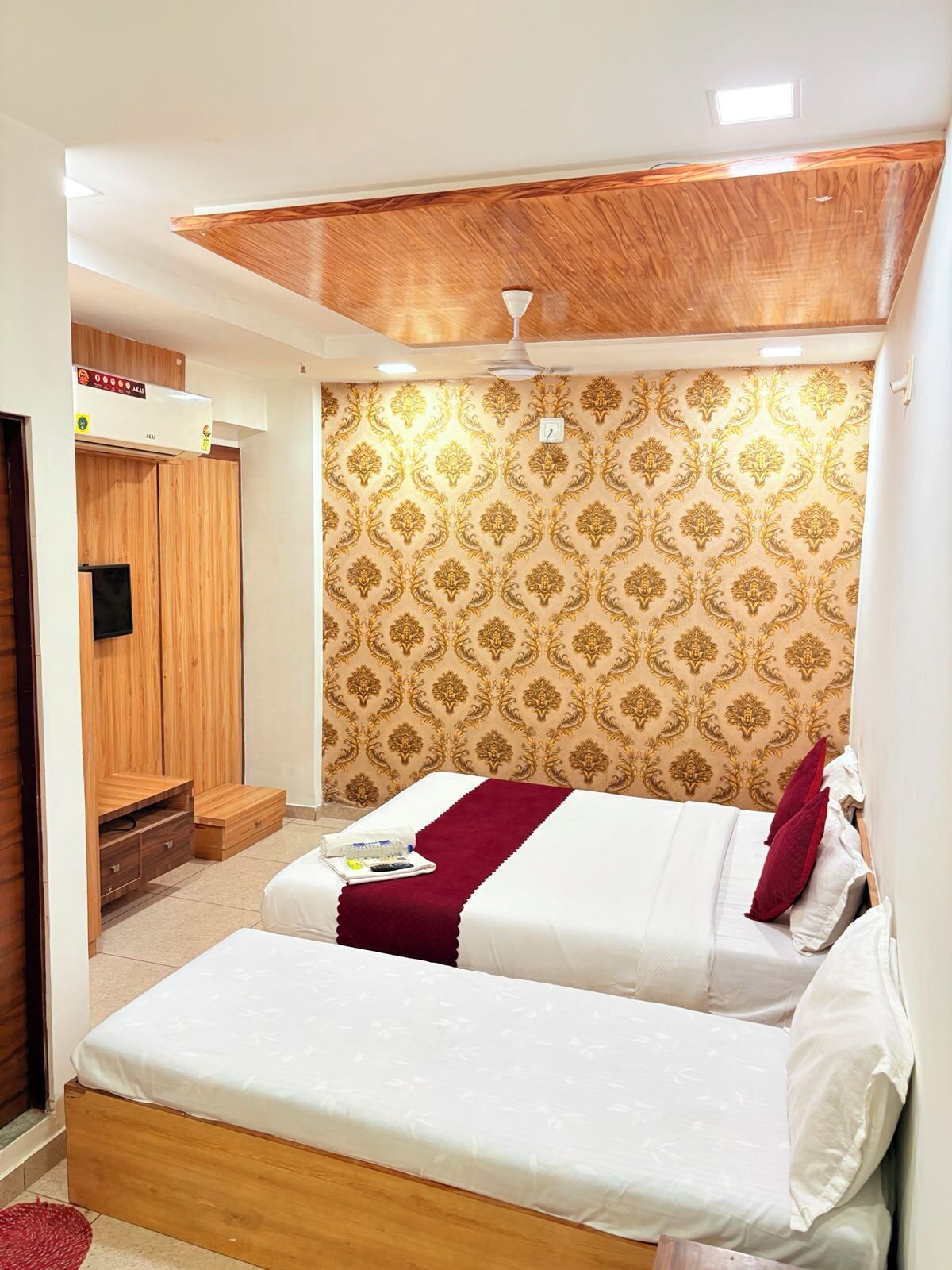 A bedroom with two beds, a wooden wardrobe, a ceiling fan, and patterned wallpaper.