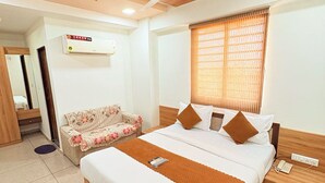 A bedroom with a bed, a ceiling fan, a window with blinds, a sofa, and a wall-mounted air conditioner. - Hotel Yuvraj (Gandhinagar)