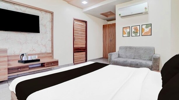 A modern hotel room with a bed, a TV mounted on the wall, a sofa, and an air conditioning unit. - Hotel Yuvraj (Gandhinagar)