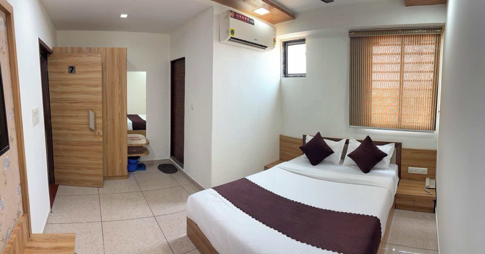 A hotel room with a bed, a desk, a wardrobe, and a window with blinds.