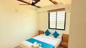 A bedroom with a bed, a ceiling fan, a window with blinds, and a wall-mounted air conditioner. - Hotel Yuvraj (Gandhinagar)