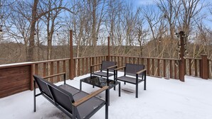 Une terrasse enneigée, dotée de mobilier d’extérieur et d’une rambarde en bois.