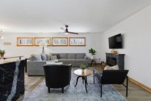 Un salon moderne comprenant un canapé, deux fauteuils, une table basse, une cheminée et un téléviseur à écran plat fixé au mur.