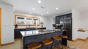 Une cuisine moderne dotée d’un îlot central, de meubles de rangement aux couleurs sombres et de tabourets en bois.