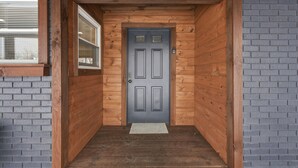 Une façade en bois avec une porte grise, une fenêtre et un mur en briques.
