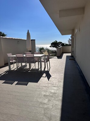 Une terrasse sur le toit, avec une table et des chaises, un parasol et une vue sur la mer.
