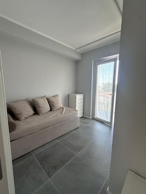 A modern living room with a grey sofa, a white cabinet, and a large sliding glass door leading to a balcony. - Stunning New beach-front apartment (Reggio Calabria)