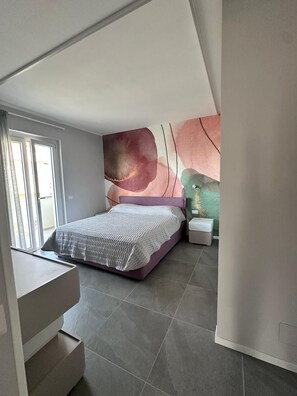 A bedroom with a bed, a nightstand, a wall-mounted shelf, and a staircase. - Stunning New beach-front apartment (Reggio Calabria)
