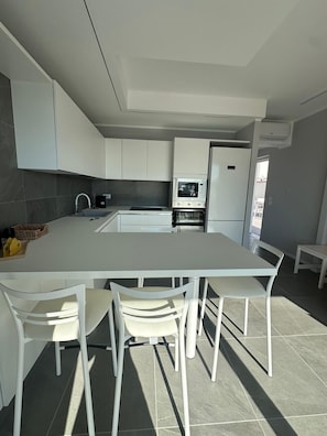 A modern kitchen with white cabinetry, a central island with chairs, a microwave, and a refrigerator. - Stunning New beach-front apartment (Reggio Calabria)