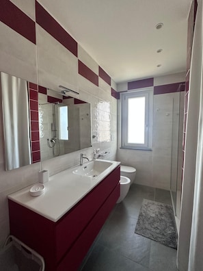 A modern bathroom with a large mirror, two sinks, a toilet, and a shower. - Stunning New beach-front apartment (Reggio Calabria)