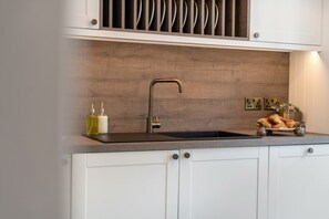 A kitchen with a modern faucet, white cabinets, and a wooden backsplash.