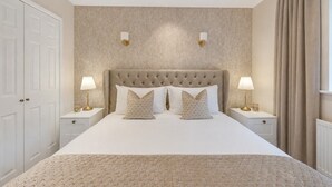 A bedroom with a large bed, two bedside tables with lamps, a tufted headboard, and a large window with curtains. - NEW! Threadfold Townhouse - Peaceful Riverside Stay - Sleeps 6 (Bolton)