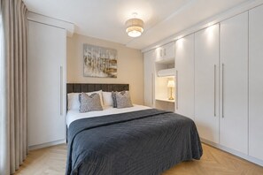 A modern bedroom with a bed, a headboard, a painting, a nightstand, and built-in cabinets.
