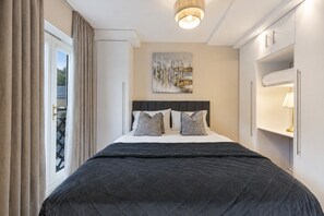 A hotel room with a bed, a painting on the wall, and a window with curtains.