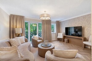 A living room with a sofa set, a round coffee table, a TV, and a balcony with curtains.
