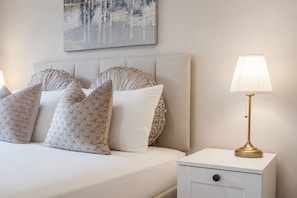 A neatly made bed with a headboard, a bedside table with a lamp, and a wall-mounted painting.