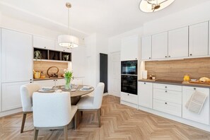 A modern kitchen with white cabinetry, a dining area with a round table and chairs, and a herringbone wood floor.