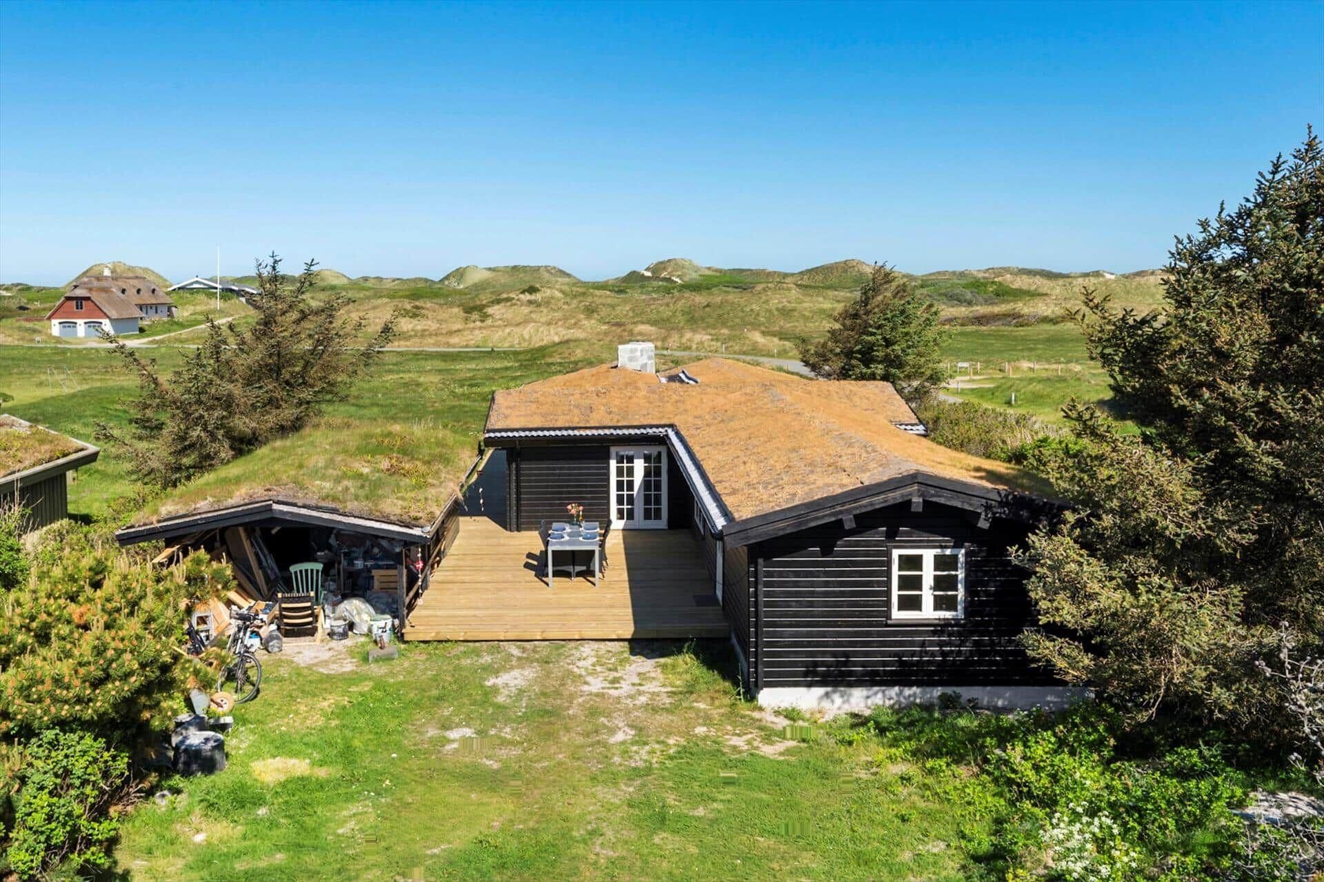 Une cabane en bois dotée d’une terrasse, entourée de verdure et de collines.
