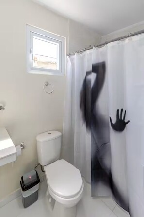 Ein Badezimmer mit Toilette, einem Fenster, einer Duschvorhang mit einem Handabdruck-Muster und einem Mülleimer.