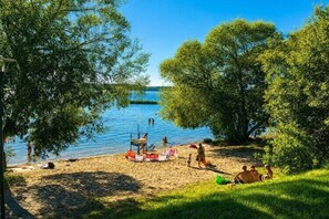A lakeside setting with a sandy beach, trees, and a clear sky. - Holiday home on Lake Żarnowieckie (Lubkowo)
