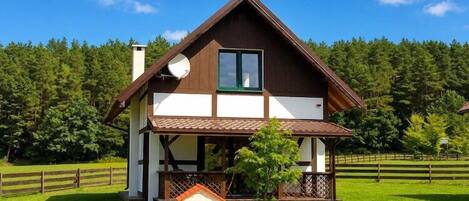 Una casa de dos pisos con un balcón, una casita de juegos y un tobogán en un césped.